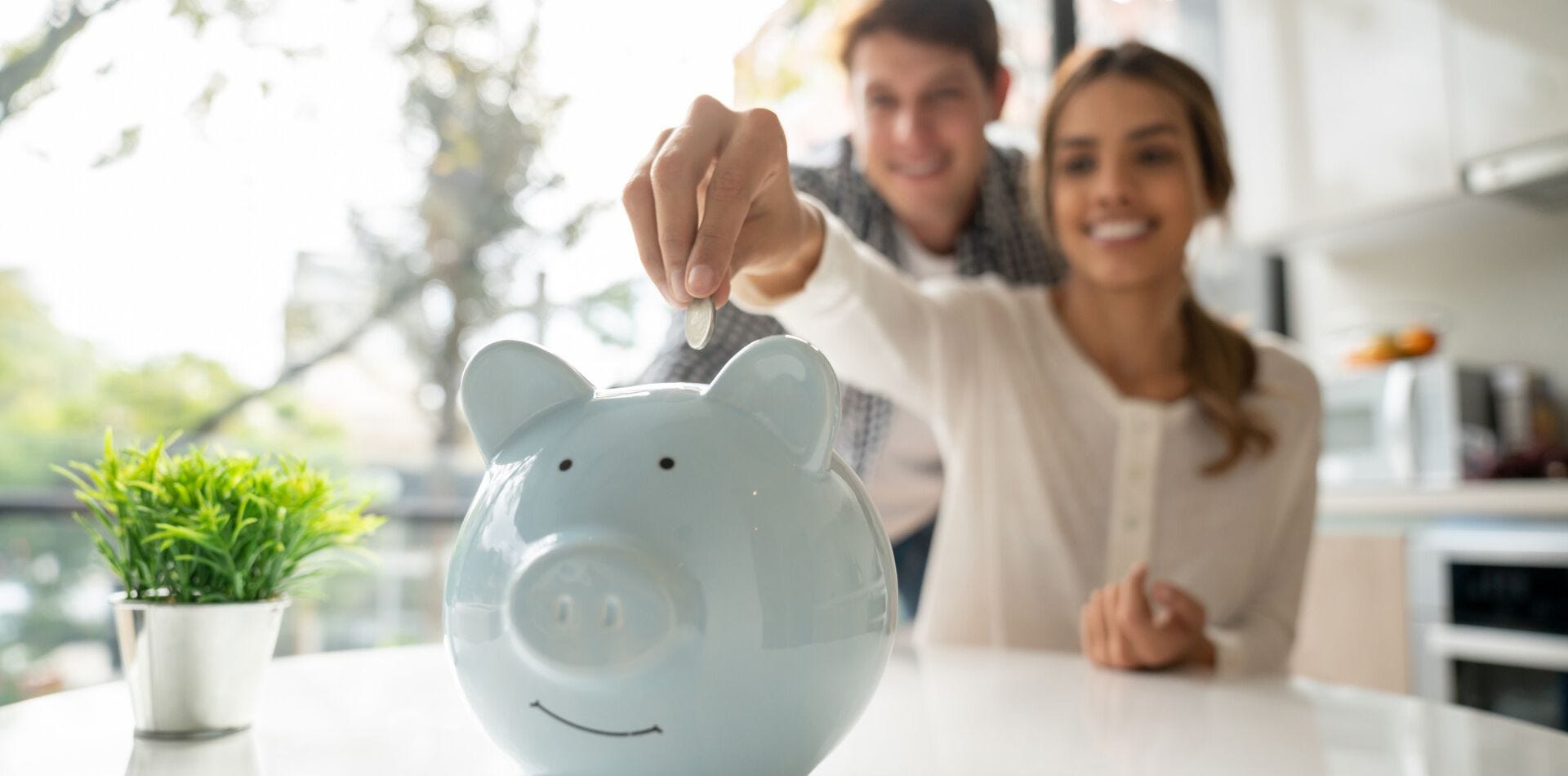 Lächelndes Pärchen steckt Geld in ein Sparschwein