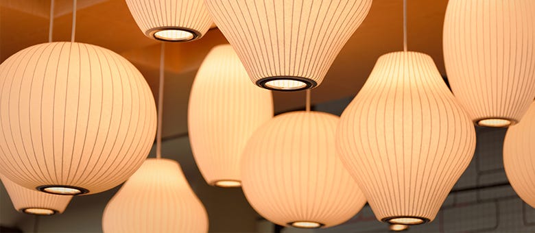 Mehrere runde und ovale Hängelampen aus hellem Material hängen von der Decke und leuchten warmes Licht aus.