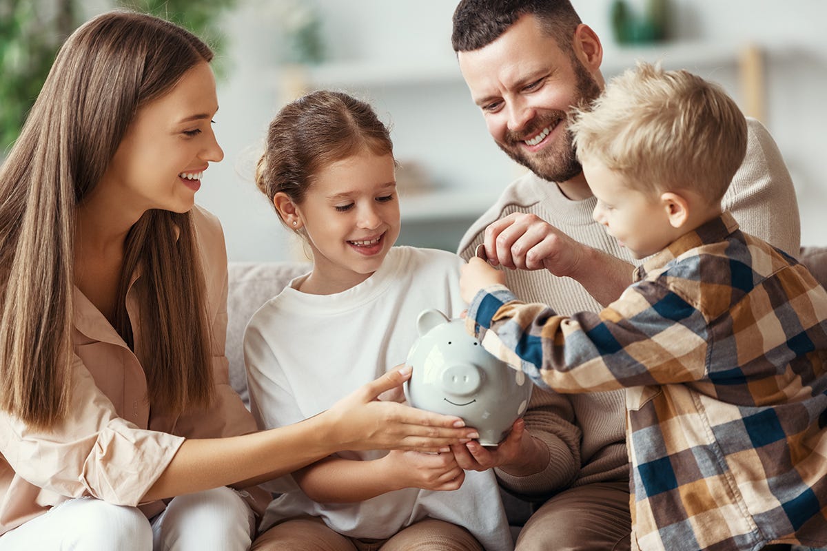 Mutter, Vater und zwei Kinder stecken lächelnd Geld in ein Sparschwein