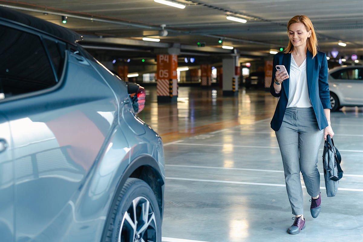 Eine Frau geht mit dem Handy in der Hand zu Ihrem Auto in der Tiefgarage
